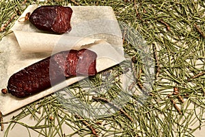 Dried sausage made of roe deer meat. Cut with slices on parchment, a large fragment. Flooring made of pine needles