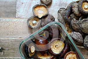 Dried shiitake mushrooms soak in water and some on a wooden background.