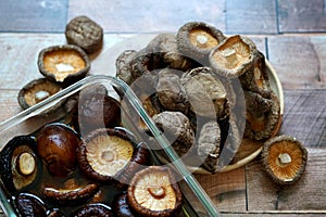 Dried shiitake mushrooms soak in water and some on a wooden plate