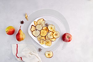 Dried sliced apple and pear on a white plate on a light gray background. Homemade fruit chips.