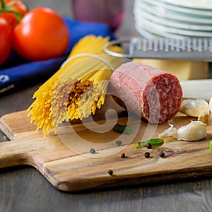 Dried spaghetti pasta with some salami on the side and tomatoes