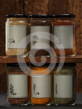 Dried spices in glass jars displayed on shelves. Assorted ground spices in bottles on wooden background.