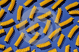 Dried spiral Italian pasta scattered on a blue background