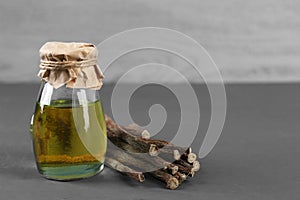 Dried sticks of licorice roots and essential oil on grey wooden table. Space for text