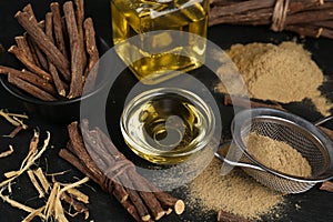 Dried sticks of licorice roots, powder and essential oil on black table