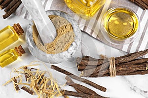 Dried sticks of licorice roots, powder and essential oil on white marble table, flat lay