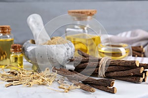 Dried sticks of licorice roots, powder and essential oil on white table, closeup