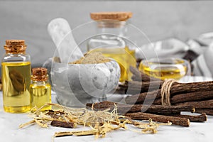 Dried sticks of licorice roots, shavings and essential oil on white table, closeup