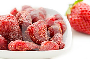 Dried strawberries in white bowl and fresh strawberry.