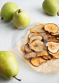 Dried sweet pear slices chips on baking paper with green ripe pears on light table.Macro