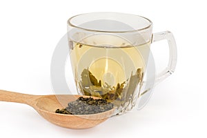 Dried tea leaves against brewed green tea in glass cup