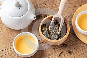 Dried tea leaves in bowl with tea set on wood table
