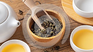 Dried tea leaves in wood bowl closeup with tea set on wooden table