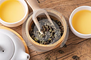 Dried tea leaves in wood bowl with scoop and tea set on wooden table