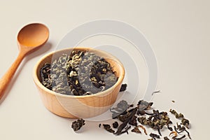 Dried tea leaves in wood bowl with spoon on beige background