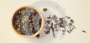 Dried tea leaves in wooden bowl on light beige background