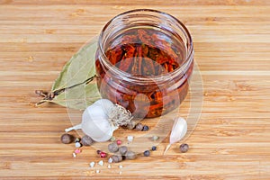 Dried tomatoes in olive oil in glass jar among spices