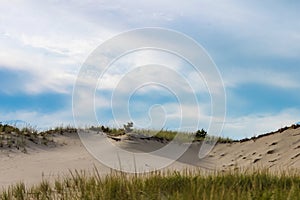 Drifted sand dunes with grass on the ridge-horizon under a blue sky