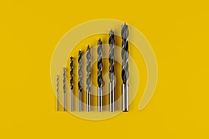 Drill bits of different sizes on yellow background,top view