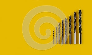 Drill bits of different sizes on yellow background,top view