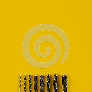 Drill bits of different sizes on yellow background,top view