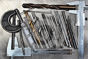 Drill bits with micrometer and calipers on metal background