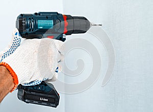 Drilling the wall with a cordless drill in protective gloves