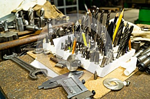 Drills, milling cutters and other metalworking tools on the table in the workshop.