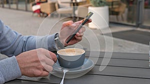 Drinking cappuccino with a phone in his hand,a man drinks coffee from a beautiful cup.