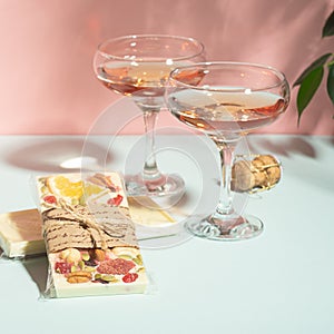 Drink champagne or wine in two elegant glasses and a bar of white chocolate. Gentle pink background bright sunlight.