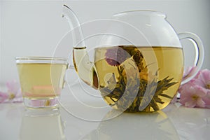 Drink of flowering tea in glass teapot with poured cup in background