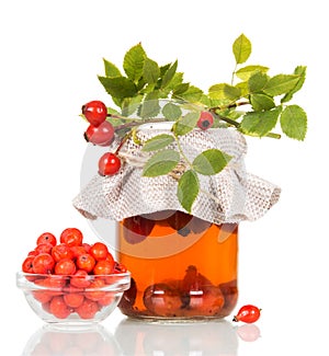 Drink from fruit of rosehip in jar, Rowan berries in bowl isolated on white