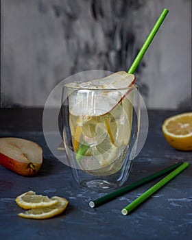 A drink for a hot summer day with ice and fruits in a transparent glass with a straw, pear and lemon fruits