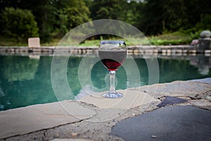 Drink in tall glass in poolside. Refreshment on summer day. Purple juice cocktail or vine. Mountain forest background.