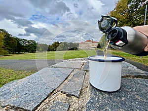 Drink tea on a hike against the background of the castle Duchcov, hands holding a thermos with a mug