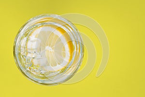 Drink, water with lemon in a glass, on a yellow background.