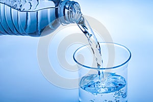 Drink water pouring in to glass over light blue background