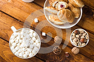 A drink in a white mug with marshmallows on top stands on a brown wooden table