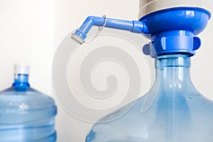 Drinking clean water at home. Close up tap view of large blue pump cooler bottle mechanism for house or office use. Two bottles