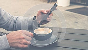 Drinking coffee with a smartphone in his hands,a man enjoying a cup of cappuccino in a cafe.
