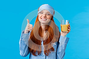 Drinking fresh juice is healthy and good. Cute glamour redhead caucasian female in sleep mask and nightwear, tilt head