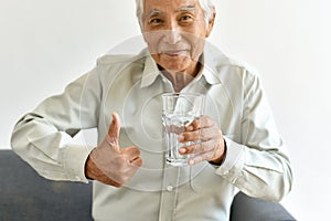 Drinking fresh water is good healthy habit for old man, Elderly smiling asian man show thumb up to glass of purified water. photo