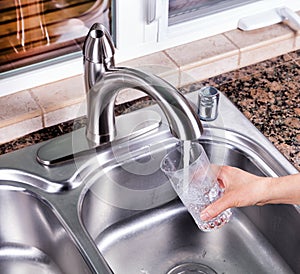 Drinking glass being filled up with tap water from kitchen faucet