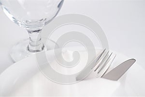 Drinking glass and cutlery into white napkin on white plate