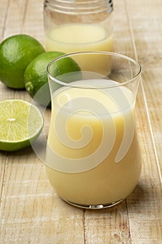 Drinking glass with lime juice and fresh green limes on the table