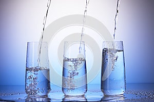 Drinking glasses with reflection in drops. Water pouring