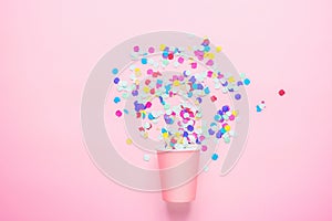Drinking Paper Cup with Multicolored Confetti Scattered on Fuchsia Background. Flat Lay Composition. Birthday Party Celebration