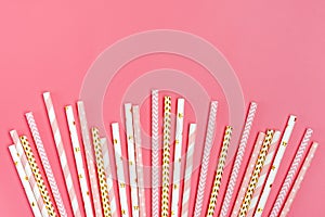 Drinking paper straws for party with golden, white, pink stripes on pink pastel background