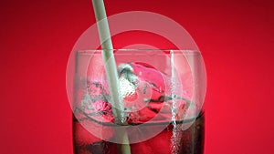 Drinking soft drink in glass with ice cube on red background. Cola or refreshment.