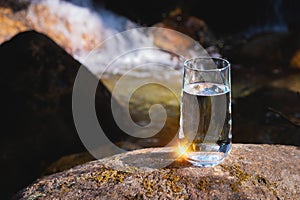 drinking transparent water in a glass glass stands on a stone outdoors in a forest in nature, a waterfall rages on a